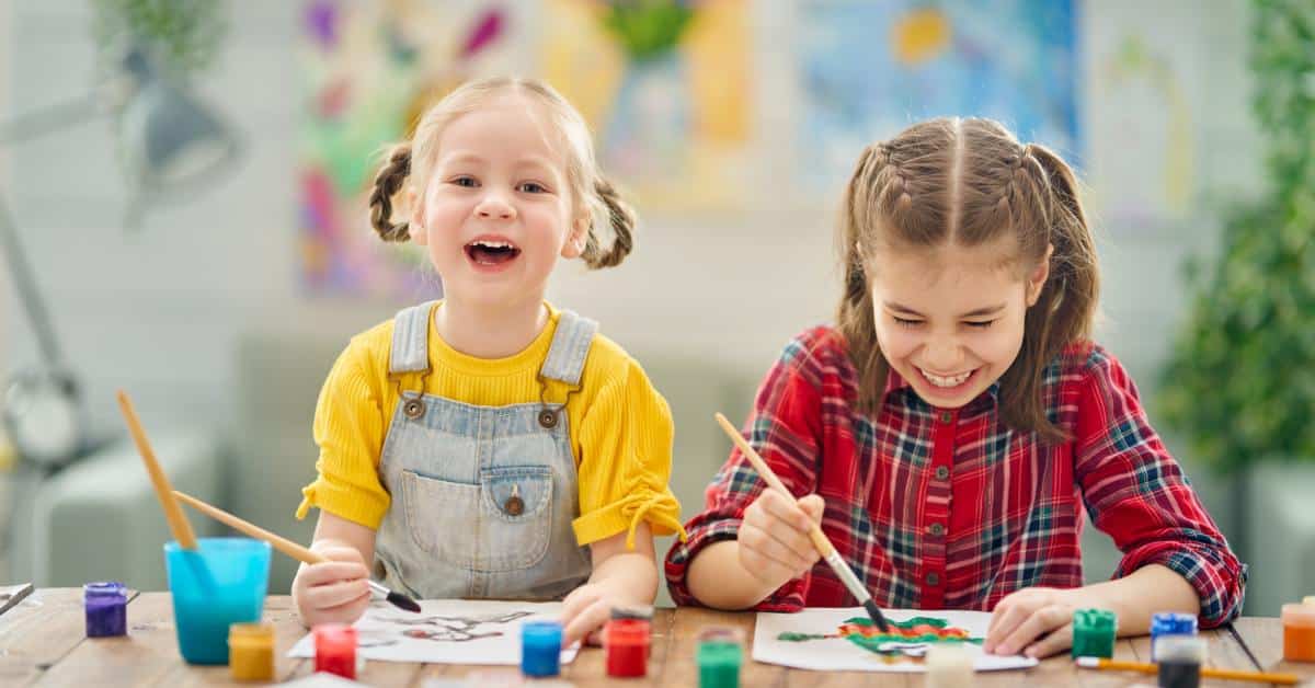 Two children, one wearing a yellow shirt and the other wearing a red one, are sitting next to each other.