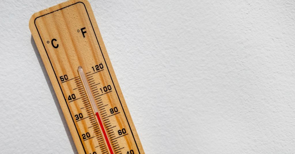 A thermometer is on a white surface. The mercury in the glass tube indicates the temperature is 30 degrees Celsius.