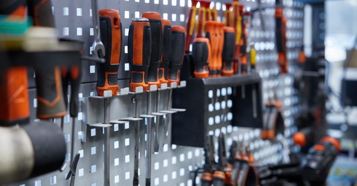 Different tools are hanging on a wall mounted tool board. Most of the tools are screwdrivers.